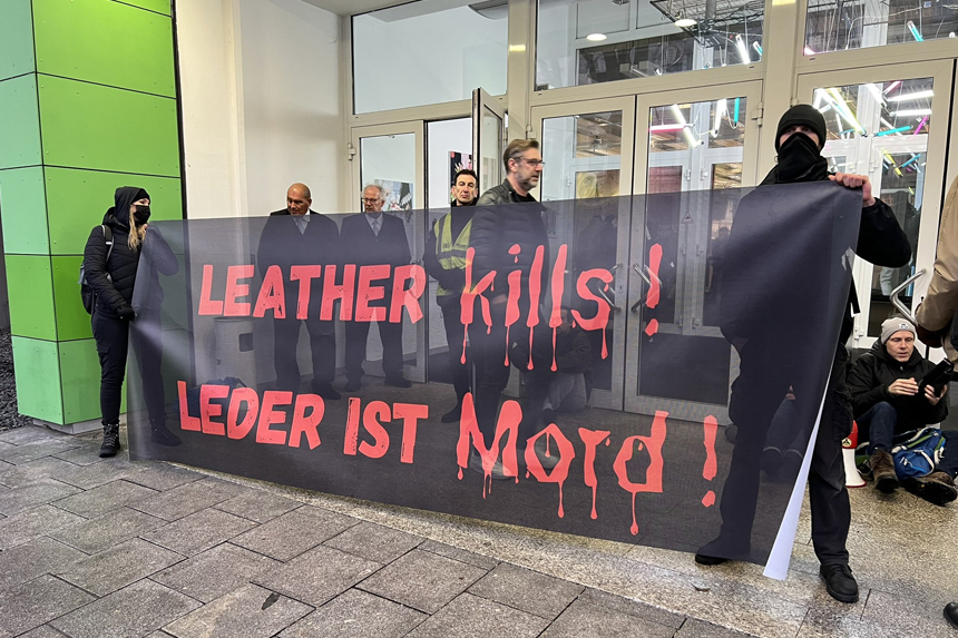 Menschen blockieren den Eingang der Ledermesse in Offenbach. Sie tragen ein Transparent mit der Aufschrift Leather kills bzw. Leder ist Mord. Im Hintergrund ist das Gebäude der Messe Offenbach zu sehen.